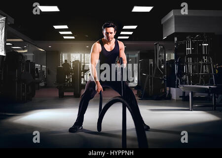 Man is doing exercises working out with rope in the gym. Stock Photo