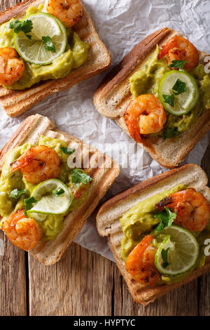 tasty Mexican sandwiches with guacamole, prawns and lime close-up on the table. Vertical view from above Stock Photo