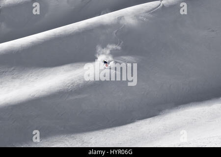 Courmayeur, Italy - January 16, 2017: Fresh first tracks put down by single lone skier coming down mountain ridge spraying new fallen snow in turns Stock Photo