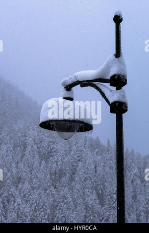 Traditional wrought iron lamppost covered in snow from storm turning forest and valley snowy white Stock Photo