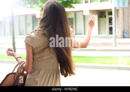 Stylish young woman waving for a taxi cab in the city Stock Photo
