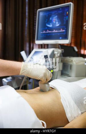 Doctor in a hospital diagnostic room doing an ultrasound of a patient abdomen with convex probe. Modern medical equipment, preventional medicine and h Stock Photo