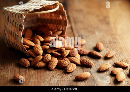 Whole almonds falling out of a small basket. A pile of almonds on a wooden surface. Stock Photo