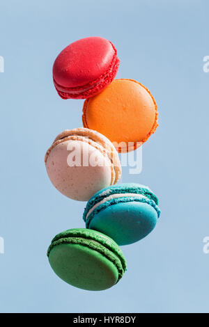 Different types of macaroons in motion falling on light blue background. Sweet and colourful french macaroons falling or flying in motion. Stock Photo