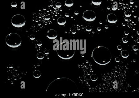 Round shaped water droplets on glass surface. Dark background behind. Stock Photo