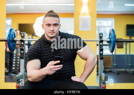 Young handsome man using phone while having exercise break in gym. Stock Photo
