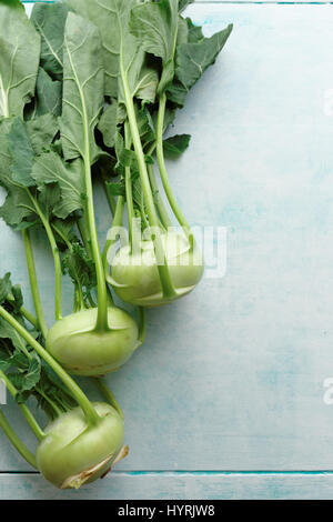 Fresh kohlrabi with green leaves. A bunch of freshly harvested kohlrabi on a blue table. Stock Photo