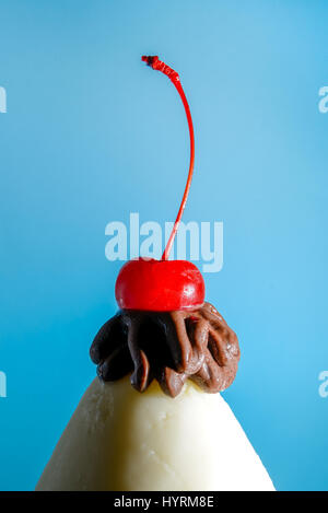 Ice cream cone with chocolate and a cherry on top in front of a blue background. Stock Photo