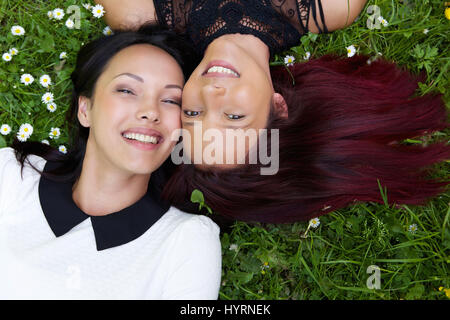 Portrait of a two happy sisters lying on grass outdoors Stock Photo