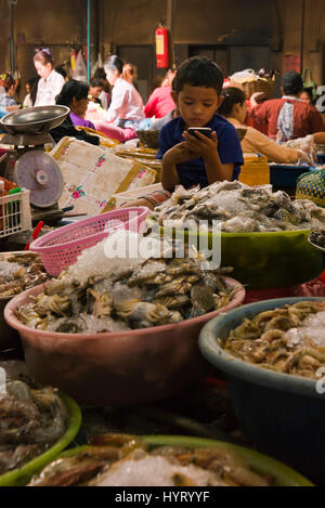 Vertical portrait of a young boy playing with his phone inside the Wet Market in Siem Reap, Cambodia. Stock Photo