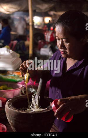 Vertical portrait of a lady mixing ingredients for a papaya salad in Cambodia. Stock Photo