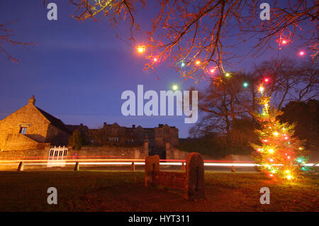 Christmas decorations by the wooden stocks on the  village green in Eyam, Peak District National Park, England UK Stock Photo