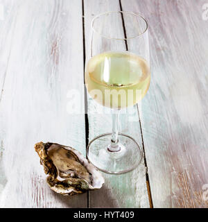 A square photo of freshly opened oysters with a glass of white wine, on a blurred wooden background texture with copyspace Stock Photo