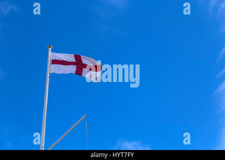 St Georges flag flying against a blue sky from a gold topped flagpole. Stock Photo