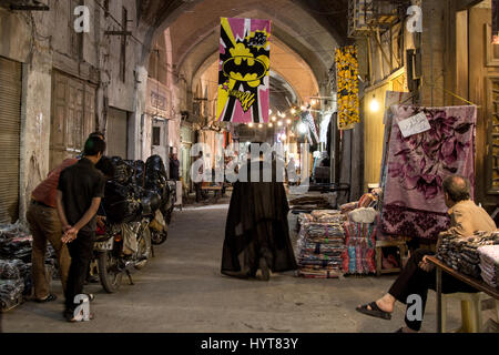 ISFAHAN, IRAN - AUGUST 20, 2016: Imam passing under a Batman logo in Isfahan bazaar  Picture of an Iranian imam from the back walking under a Batman l Stock Photo