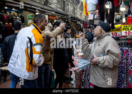 ISTANBUL, TURKEY - DECEMBER 28, 2015: Old merchant trying to sell anti stress head massage devices to laughing men near the spice bazaar, on the Europ Stock Photo