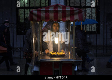 ISTANBUL, TURKEY - DECEMBER 30, 2015: Picture of an young chestnut seller on a winter evening under the snow  Young chestnut seller near Eminonu squar Stock Photo