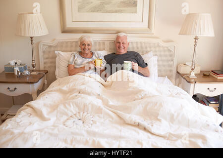 Content senior couple sitting in bed together drinking coffee Stock Photo