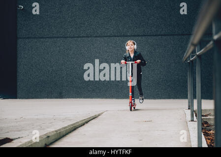 Girl wearing black leather jacket driving red scooter and listening to music on headphones Stock Photo