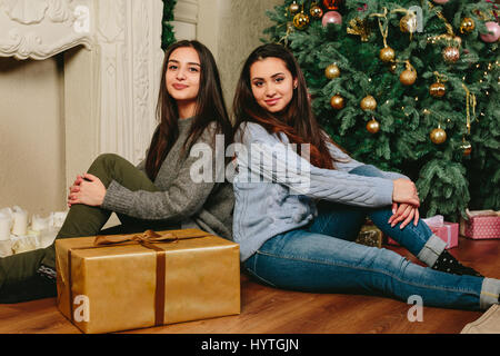 Two beautiful young girls sitting on the floor near a Christmas tree. studio horizontal photo Stock Photo