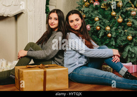 Two beautiful young girls sitting on the floor near a Christmas tree. studio horizontal photo Stock Photo