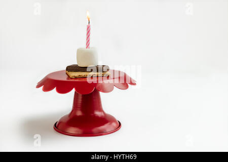 S'more birthday surprise on red cake plate with a pink and white lit candle to celebrate birthday by eating marshmallow, chocolate, and graham cracker. Stock Photo
