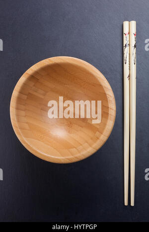 Chinese chopsticks with empty wooden bowl on sblack late. Stock Photo