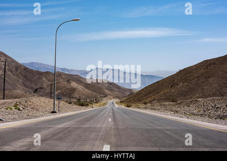 scenic road through wild, arid mountains in Oman, leading to Wadi Bani Khalid, a nature escape with blue skies and copy space, a travel destination Stock Photo