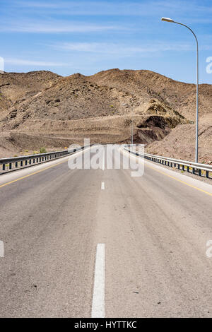 Empty road winding through arid mountains and a wadi in Oman, leading to Wadi Bani Khalid, a serene travel destination and nature escape, copy space Stock Photo