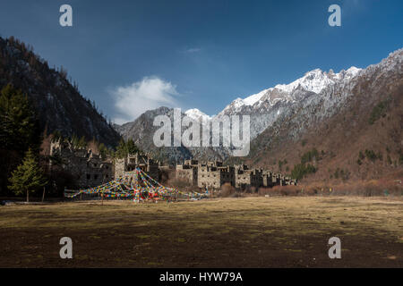 Beautiful Tibetan village in traditional stone with prayer flags, snow capped mountains and blue sky, Jiuzhaigou National Park, China Stock Photo