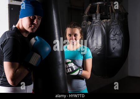 Young female spoty boxer in boxing gloves training with her trainer and boxing punching bag in a gym Stock Photo