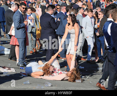 Racegoers lying on the ground on Ladies Day of the Randox Health Grand National Festival at Aintree Racecourse. Stock Photo