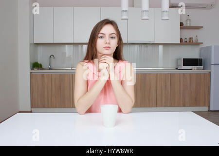 Smiling woman which sitting on kitchen with cup of coffee and looking at camera Stock Photo