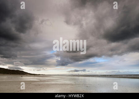 Moody, stormy and grey skies looming over wet sand at low tide on an empty beach at Saltburn in North Yorkshire Stock Photo