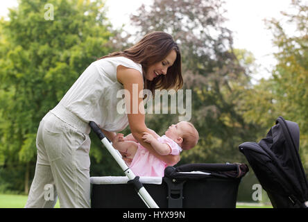 Side view portrait of a mother putting baby into pram Stock Photo