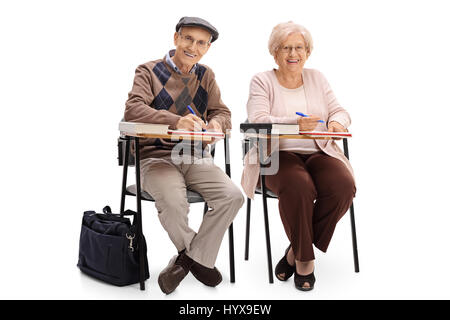 Two elderly students sitting in school chairs and taking notes isolated on white background Stock Photo