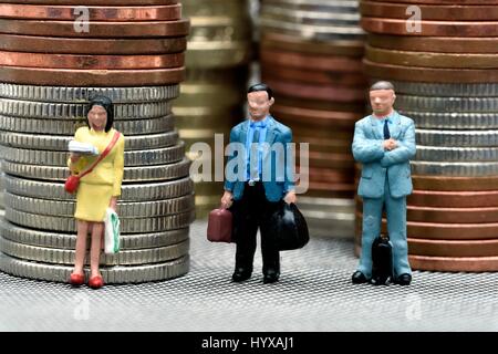 Miniature figurines standing in front of stacks of coins. Stock Photo