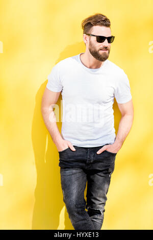 Colorful portrait of a handsome man dressed in white t-shirt and jeans on the yellow background Stock Photo