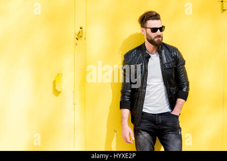 Colorful portrait of a handsome man dressed in white t-shirt, jacket and jeans on the yellow background Stock Photo