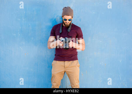 Portrait of a stylish photographer dressed casual in t-shirt and hat standing with camera on the blue background Stock Photo