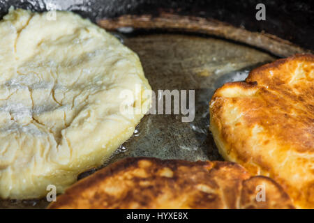 Process of frying cottage cheese fritters or pancakes in sizzling oil in old iron cast pan, rural style, close up Stock Photo