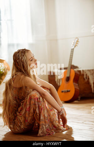 Portrait of young blonde hippie woman sitting on floor and looking away Stock Photo