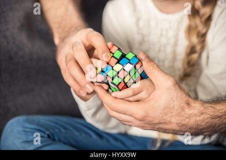 Pensive father and daughter playing with cube on couch Stock Photo