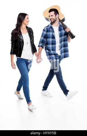 Smiling young couple holding hands and looking at each other while walking with guitar Stock Photo