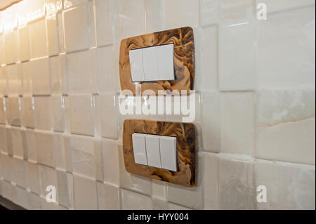 Closeup detail of two rocker light switch sockets on a white tiled kitchen wall Stock Photo
