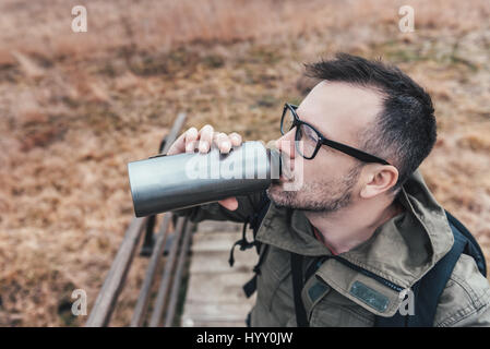 Hiker standing on wooden bridge and drinking water Stock Photo