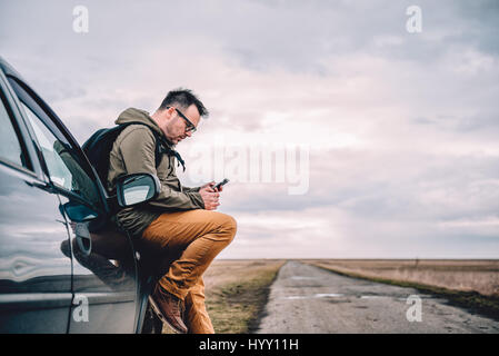 Man sitting on the car and using smart phone Stock Photo