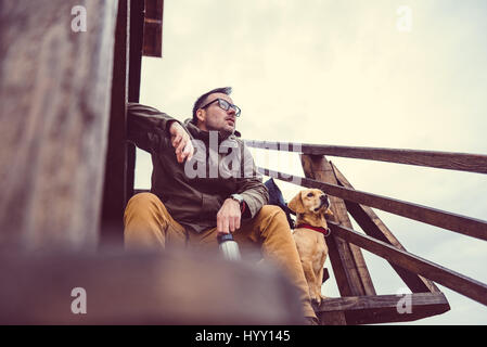 Hiker and dog sitting on the stairs of hikers rest cabin Stock Photo