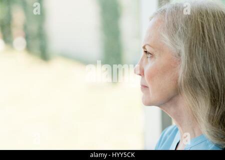 Senior woman looking through window. Stock Photo