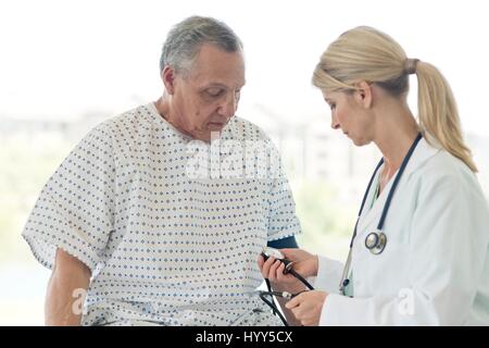 Female doctor taking senior man's blood pressure. Stock Photo